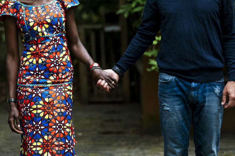 Cropped colorful woman wearing african dress holding hands man