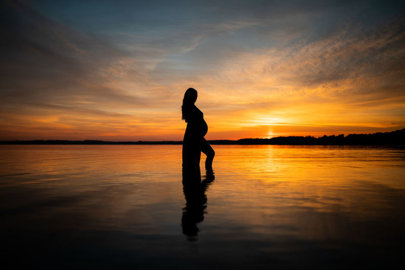 Silhouette woman standing on lake against sky during sunset