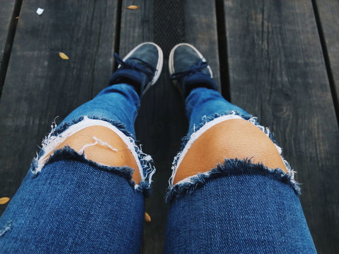 Low section of woman wearing torn jeans on boardwalk