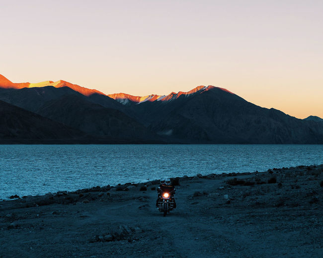 People riding motorcycle by lake against at sunset