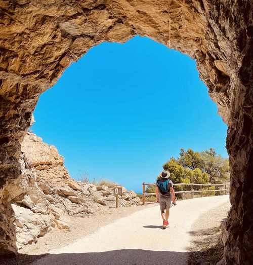 Rear view of a man walking on tunnel rock against clear blue sky