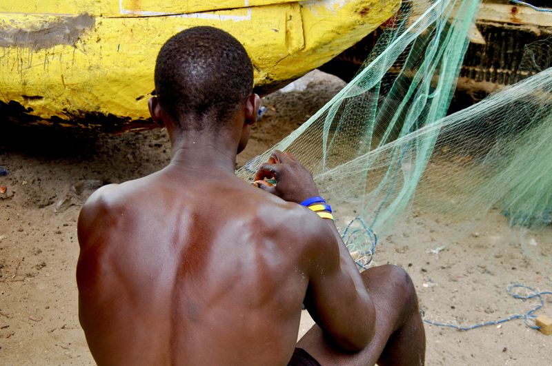 Rear view of shirtless man knitting fishing net