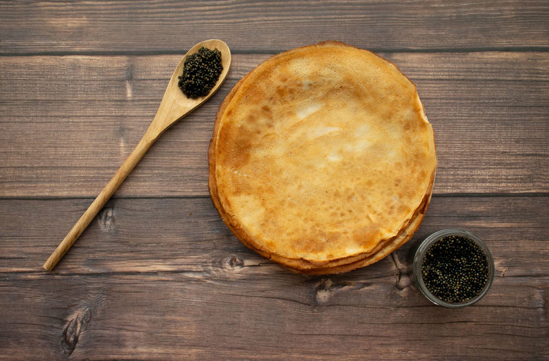 Pancakes and black caviar on the wooden background