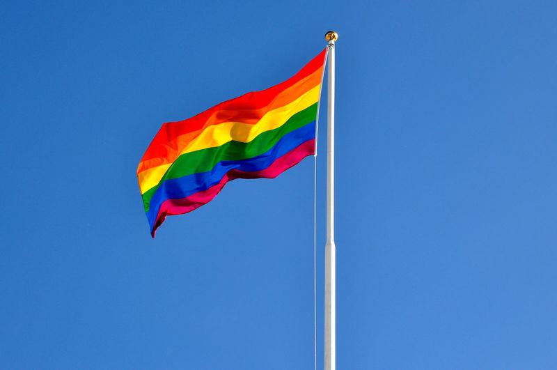 Low angle view of rainbow flag against clear blue sky