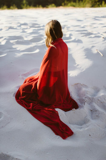 Woman in red coat sitting on the sand