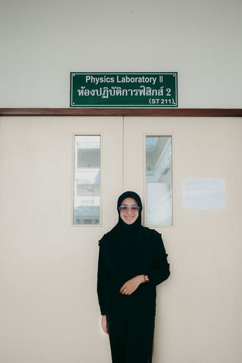 Portrait of young woman standing against door