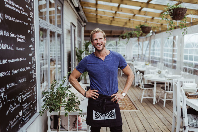 Portrait of smiling male owner with hand on hip standing in restaurant