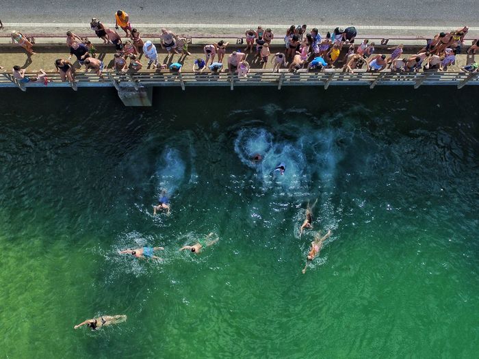 High angle view of people on bridge with swimmers in river 