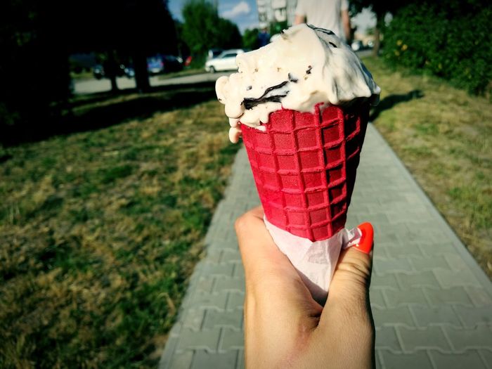 Cropped image of hand holding ice cream on footpath