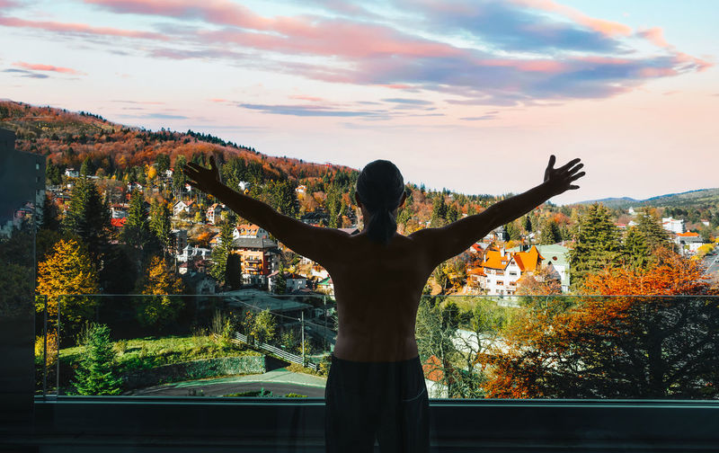 Rear view of man with arms outstretched standing against trees