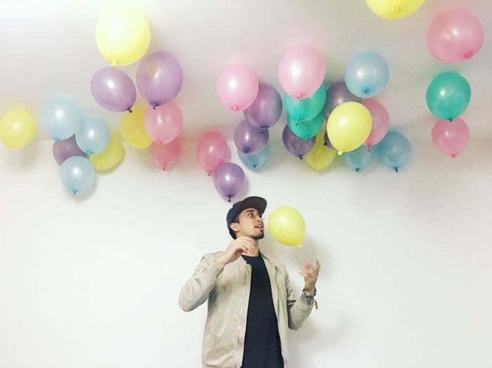 Young man with helium balloons standing under ceiling