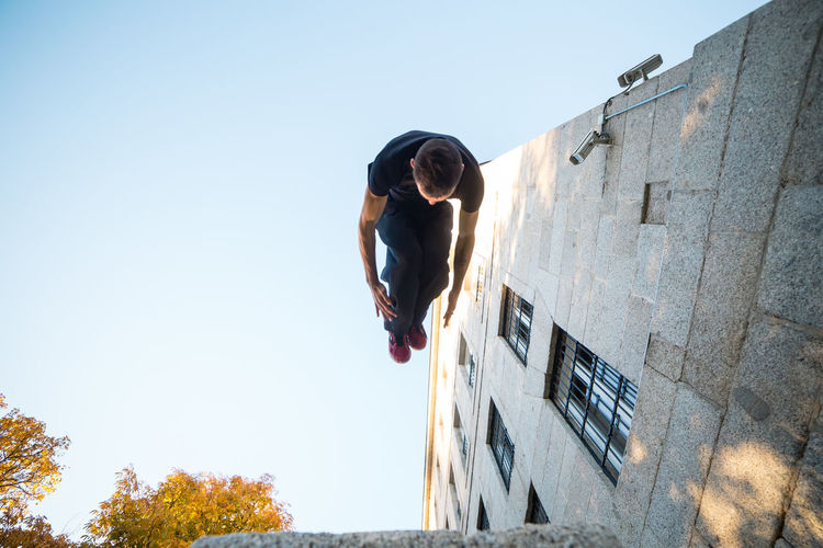 Low angle view of man jumping by buildings against clear sky