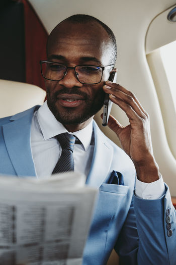 Male entrepreneur with newspaper talking on smart phone in private jet