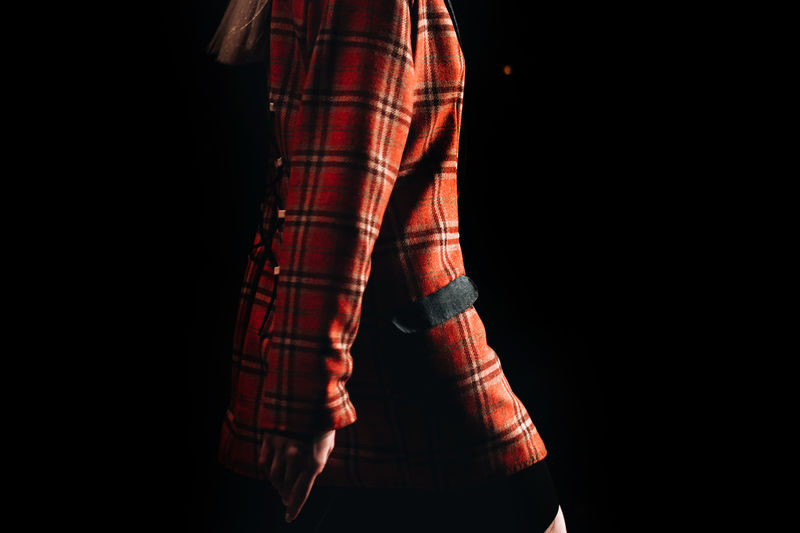 Part of a female figure wearing a checkered red jacket on black background. runway fashion show