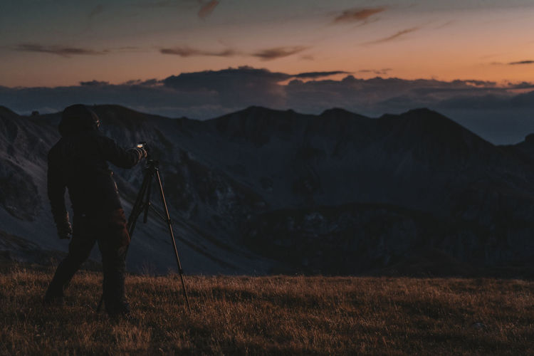 Man photographing on field against sky during sunset