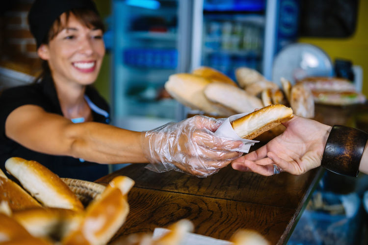 Smiling baker giving fresh bread to customer at counter in bakery