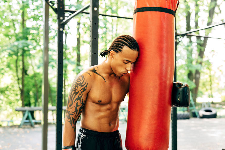 Tired athlete holding punching bag outdoors