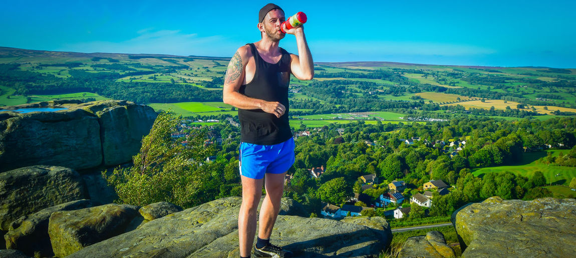 Man drinking drink while standing on cliff against green landscape