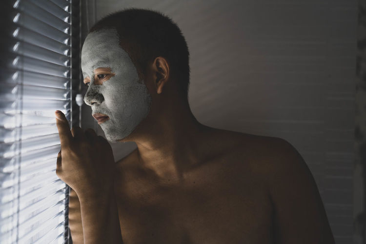 Young man looking through blinds at home
