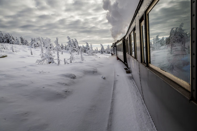 Train on snow covered field by trees against sky