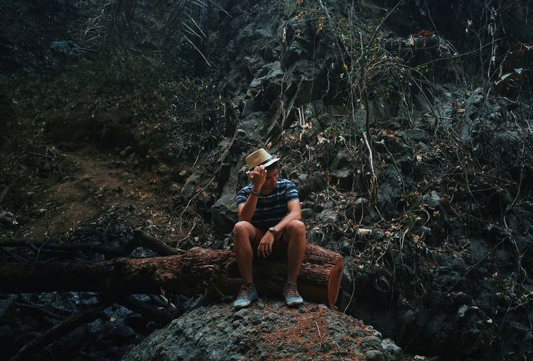 Thoughtful young man sitting on fallen tree trunk in forest