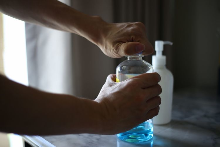 Close-up of hand holding glass bottle. opening an alcohol liquid for cleaning.