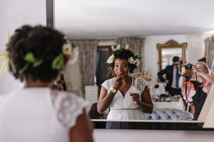 Reflection of bride applying lipstick while standing in front of mirror