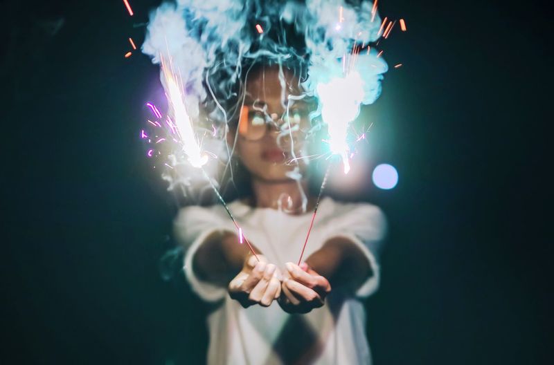 Woman holding lit sparklers at night