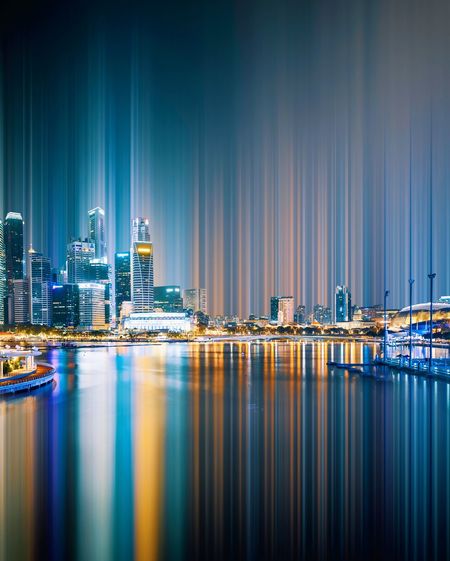 Illuminated city by river against sky at night
