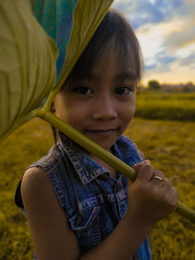 Portrait of smiling girl holding leaf on field