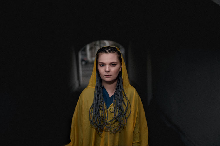 Portrait of young woman wearing raincoat while standing in tunnel
