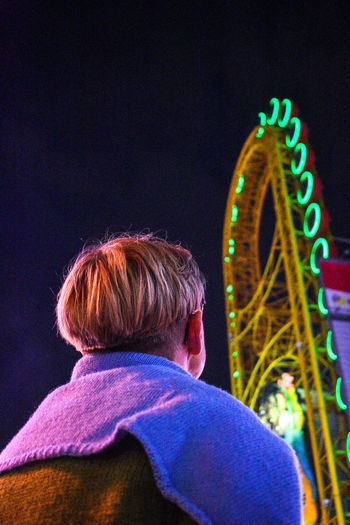 Low angle view of man standing against illuminated amusement park ride at night