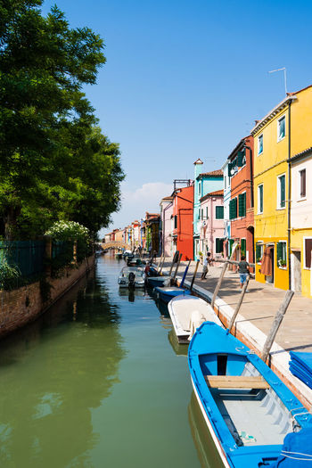 Boat moored in canal by buildings against sky in city