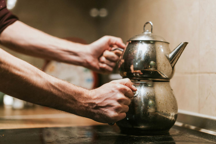 Dirty metal teapot held in hand by caucasian male hand kitchen background stock photo