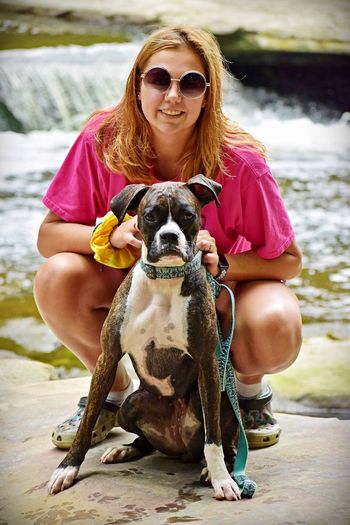 Portrait of smiling young woman with dog against river