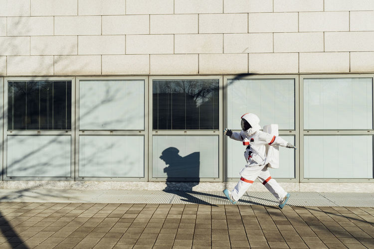 Female astronaut walking at building in city during sunny day
