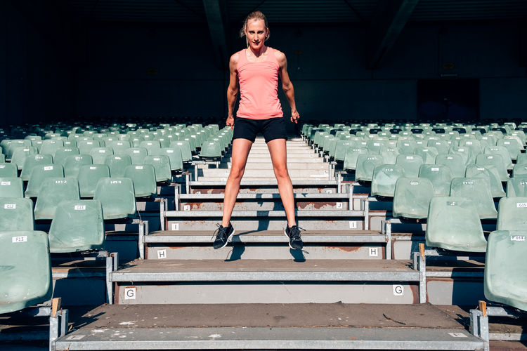 Front view of a fit and healthy woman workingout at the stadium jumping up and down the steps 