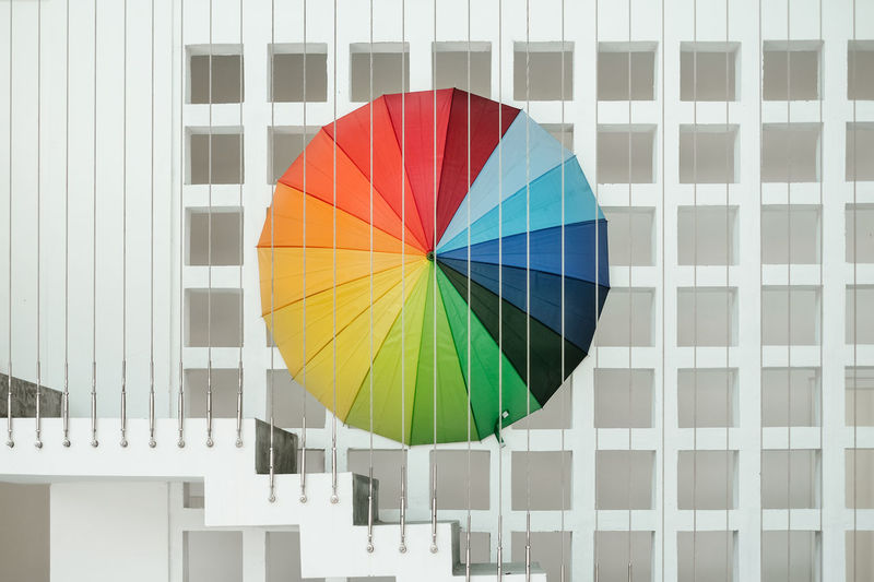 Low angle view of multi colored umbrella against white concrete wall