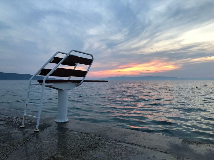 Diving board on pier by sea against sky during sunset