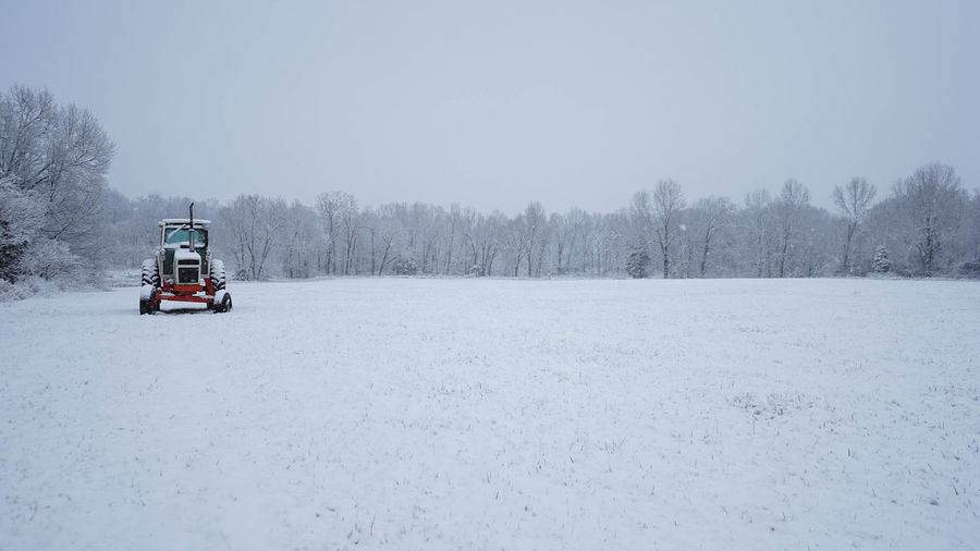 Snow covered land and trees on field against sky
