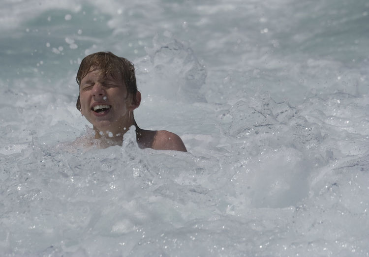 Smiling teenage boy with eyes closed swimming in sea