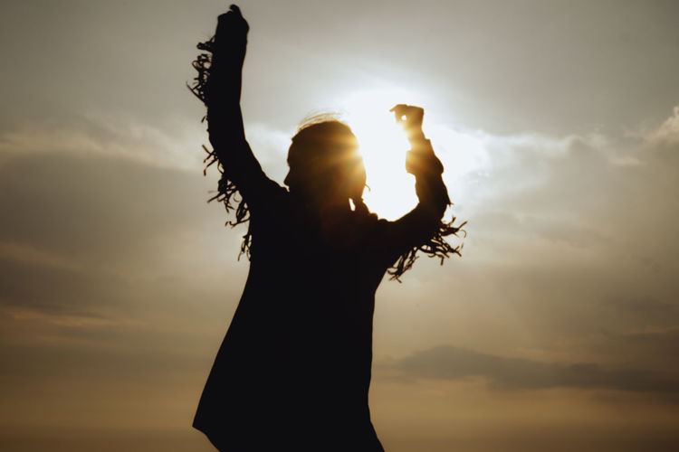 SILHOUETTE WOMAN WITH ARMS RAISED AGAINST SKY
