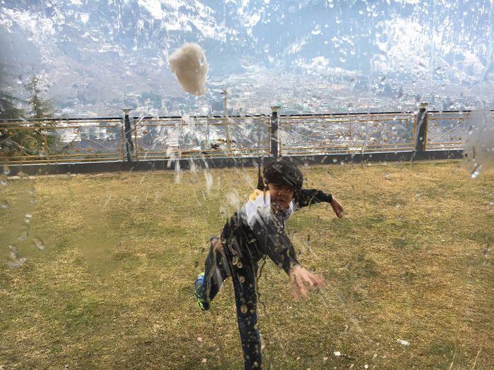Boy throwing water bomb at window while standing on grass