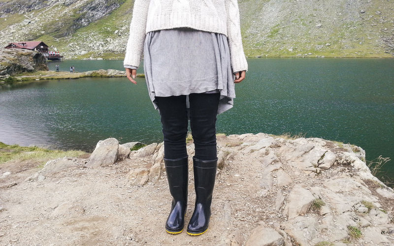 Low section of woman with rubber boot standing by lake