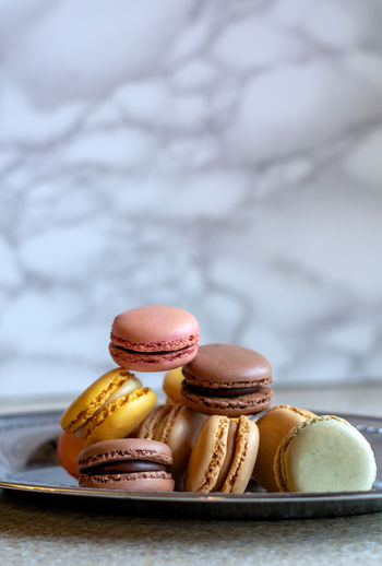 A silver tray holds a variety of elegant macarons, against a fancy marble background