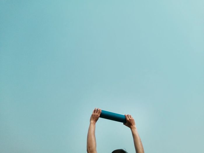 Low angle view of person hand raising loudspeaker against clear blue sky