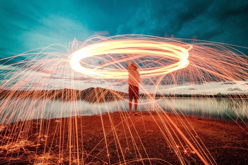 Man spinning wire wool at lakeshore during sunset