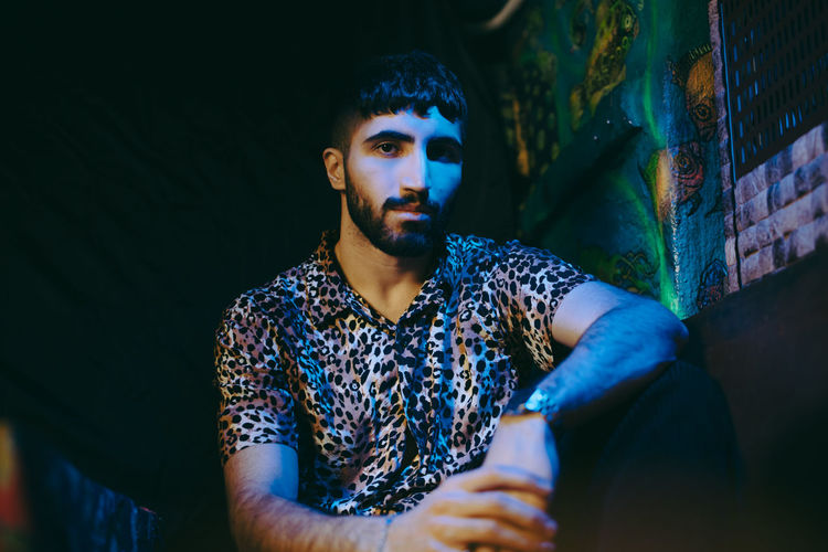 Portrait of young bearded man sitting at illuminated bar