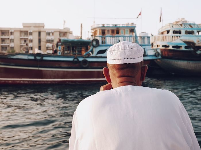 Man sitting at the shore looking at an old traditional ship in dubai creek