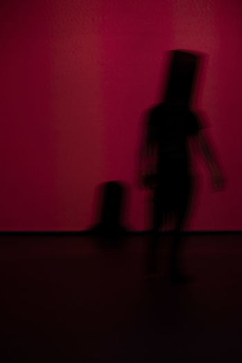 Blurred motion of silhouette man standing against red wall